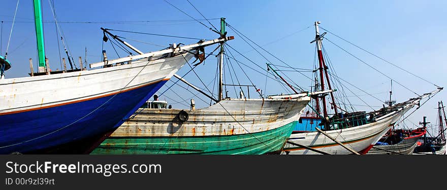 Indonesia, Jakarta: boats at Sunda Kelapa an ancient sea port; one of the most famous ports for the construction of the traditional wood boats; blue sky and colorful big wood boats. Indonesia, Jakarta: boats at Sunda Kelapa an ancient sea port; one of the most famous ports for the construction of the traditional wood boats; blue sky and colorful big wood boats