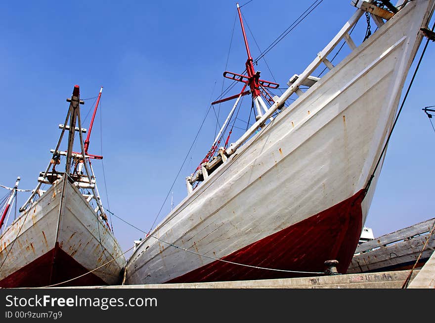 Indonesia, Jakarta: boats at Sunda Kelapa an ancient sea port; one of the most famous for the construction of the traditional wood boats; blue sky and colorful big wood boats. Indonesia, Jakarta: boats at Sunda Kelapa an ancient sea port; one of the most famous for the construction of the traditional wood boats; blue sky and colorful big wood boats