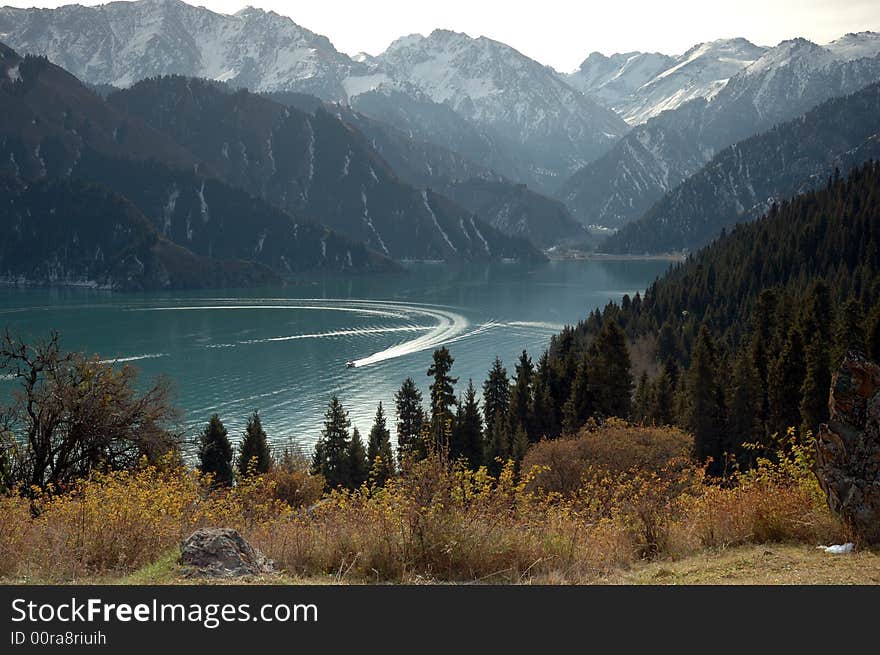 The mountain is around the lake, one yacht is passing by the surface of lake. The mountain is around the lake, one yacht is passing by the surface of lake.