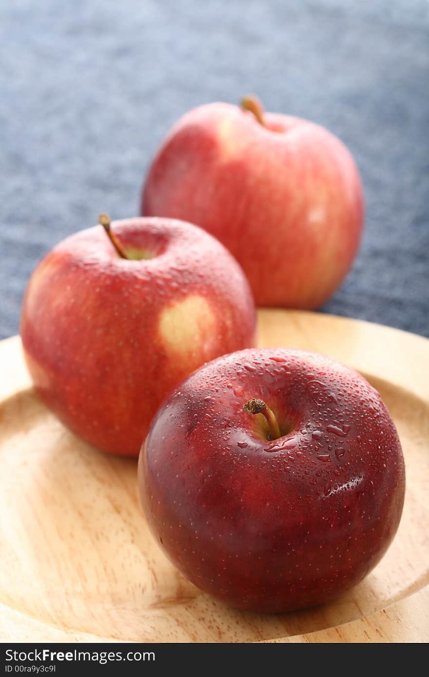 Red apples with drops of water on wooden plate with blue denim background. Red apples with drops of water on wooden plate with blue denim background