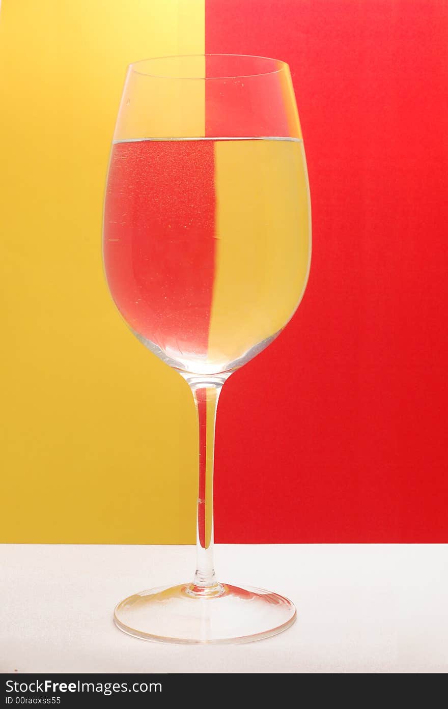 Glass of water on the background divided by yellow and red colour. Glass of water on the background divided by yellow and red colour