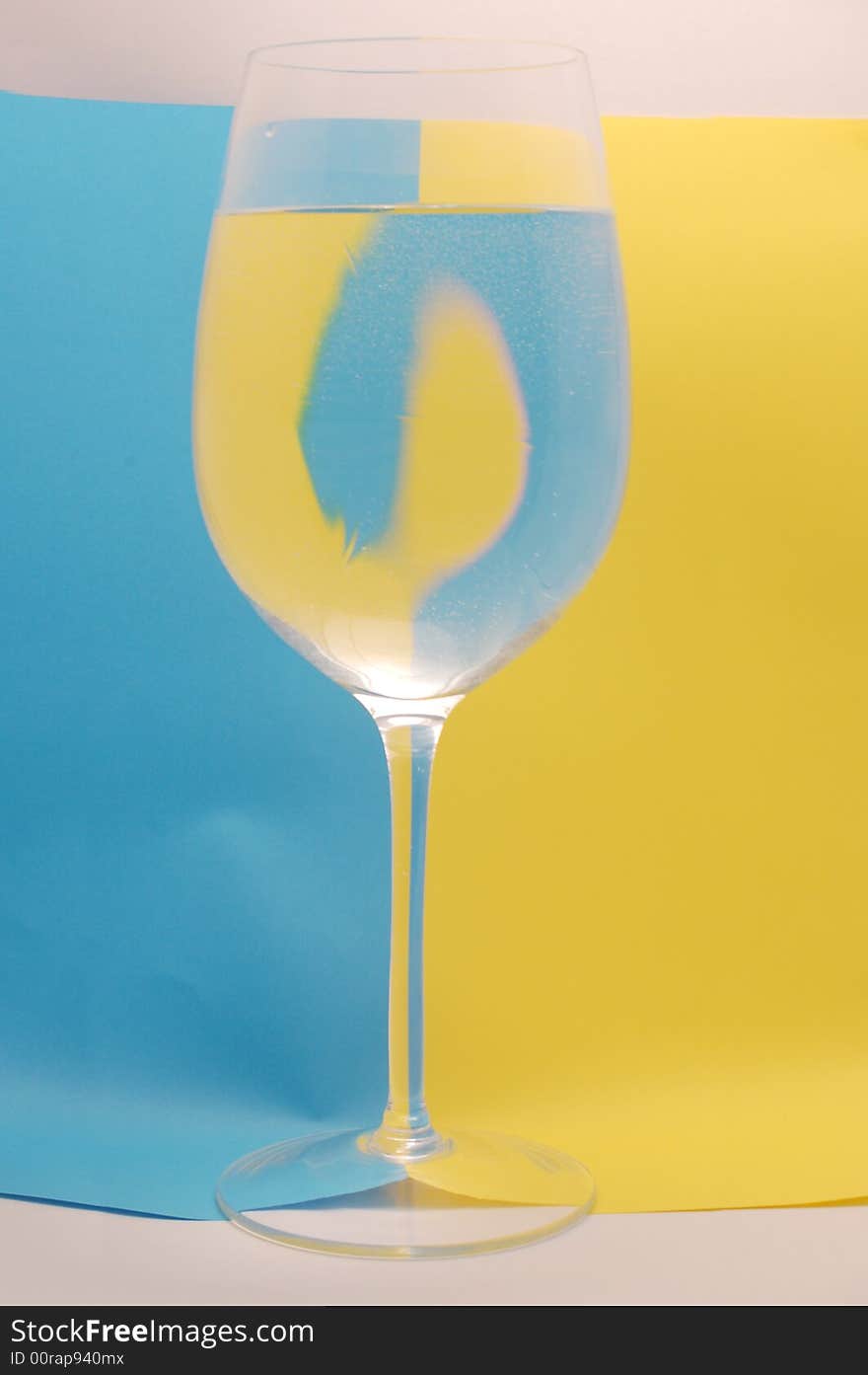 Glass of water on the background divided by yellow and blue colour. Glass of water on the background divided by yellow and blue colour