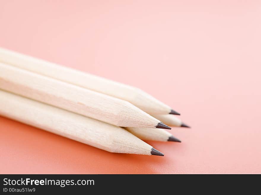 Pile of wooden pencils over a light red background. Pile of wooden pencils over a light red background