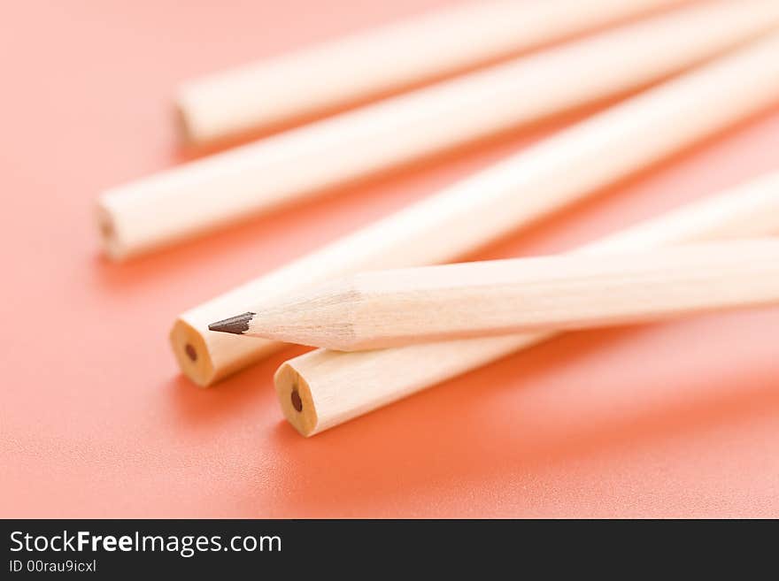 Pile of wooden pencils over a light red background. Pile of wooden pencils over a light red background