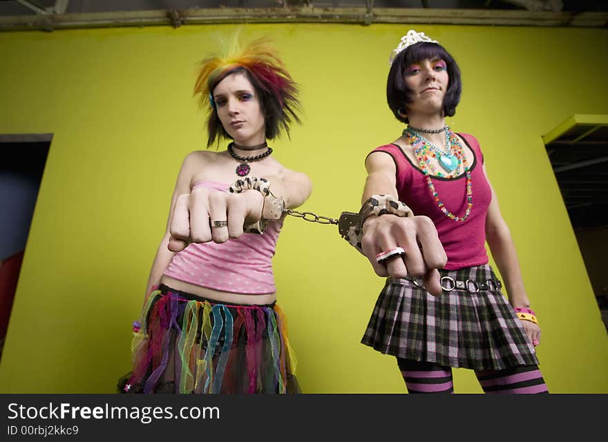 Wide angle of young punk women in front of a green wall linked by handcuffs. Wide angle of young punk women in front of a green wall linked by handcuffs