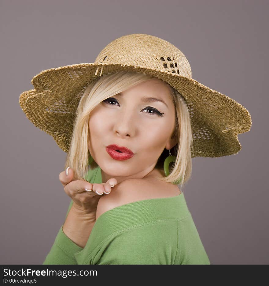 A blonde model in a green blouse and a straw hat blowing a kiss at the camera. A blonde model in a green blouse and a straw hat blowing a kiss at the camera