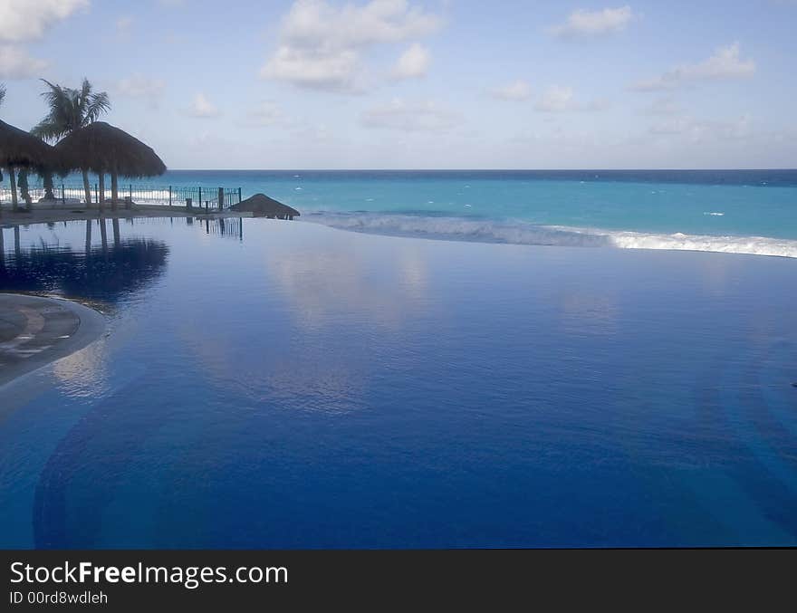 A blue lagoon type pool at a resort with ocean and clouds in background. A blue lagoon type pool at a resort with ocean and clouds in background