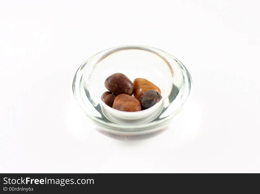 Warm colored rocks in a simple glass bowl. Exposure creates a blown out look. White background. Warm colored rocks in a simple glass bowl. Exposure creates a blown out look. White background