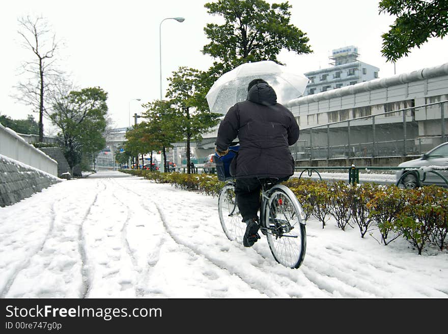 Men riding bicycle under wet snowfall on Tokyo streets, Japan, 2008. Men riding bicycle under wet snowfall on Tokyo streets, Japan, 2008