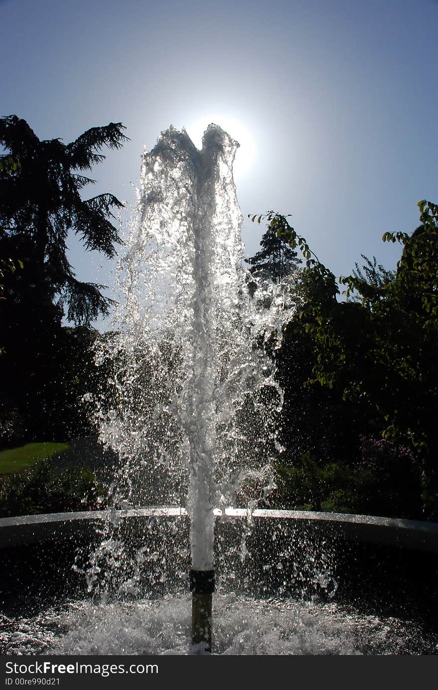 Water fountain in the garden against the sun and blue sky