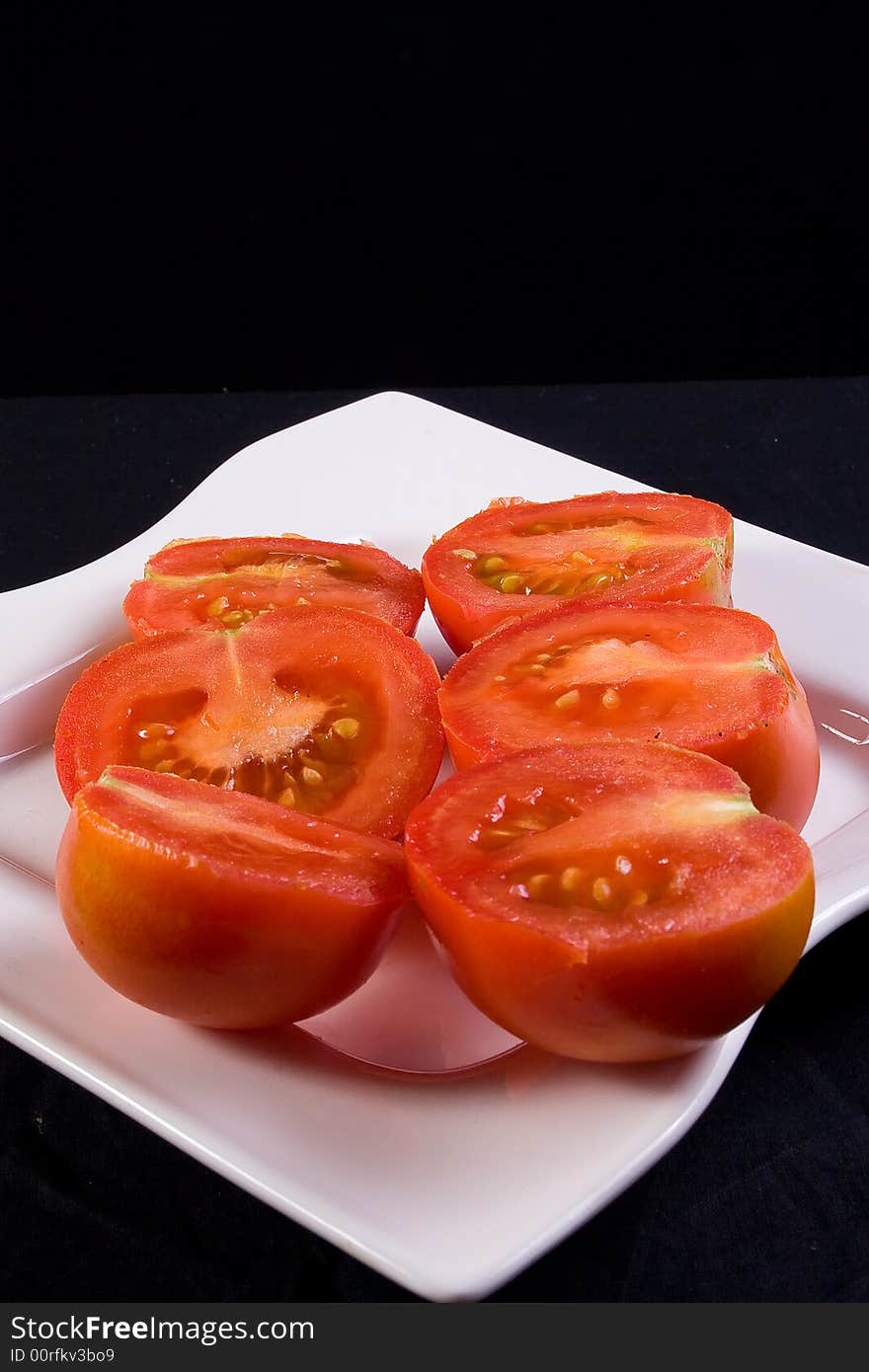 Tomato halves on white plate, black background. Tomato halves on white plate, black background.