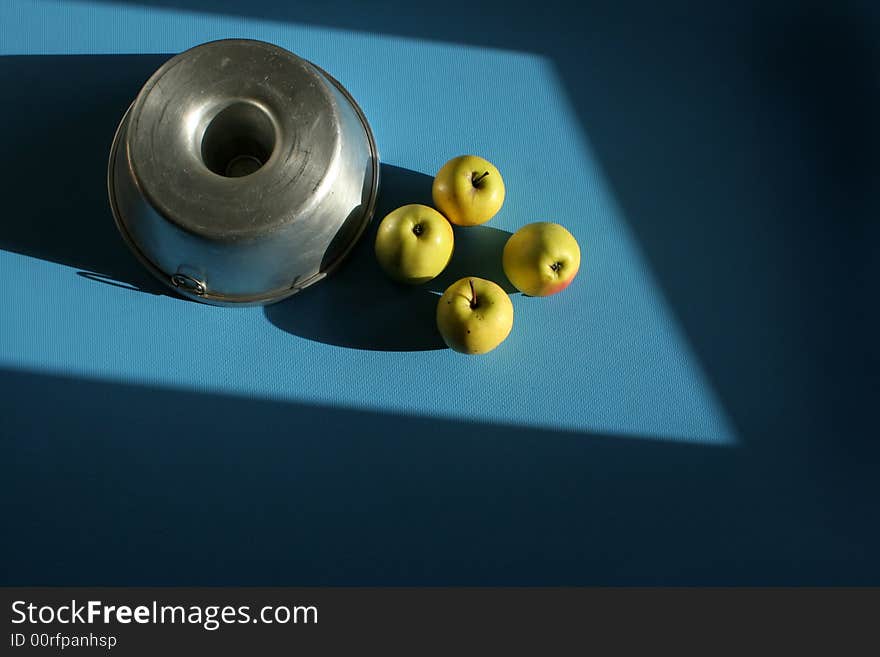 One cake tin upside down with four apples on a blue surface and direct sunlight. One cake tin upside down with four apples on a blue surface and direct sunlight