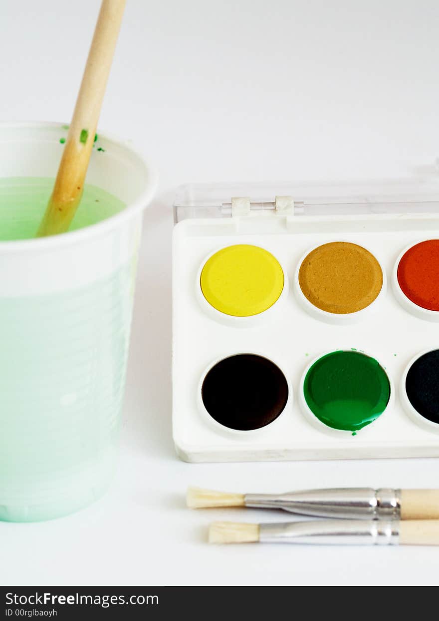 Water colors and brushes with water glass close-up studio shot on white background. Water colors and brushes with water glass close-up studio shot on white background