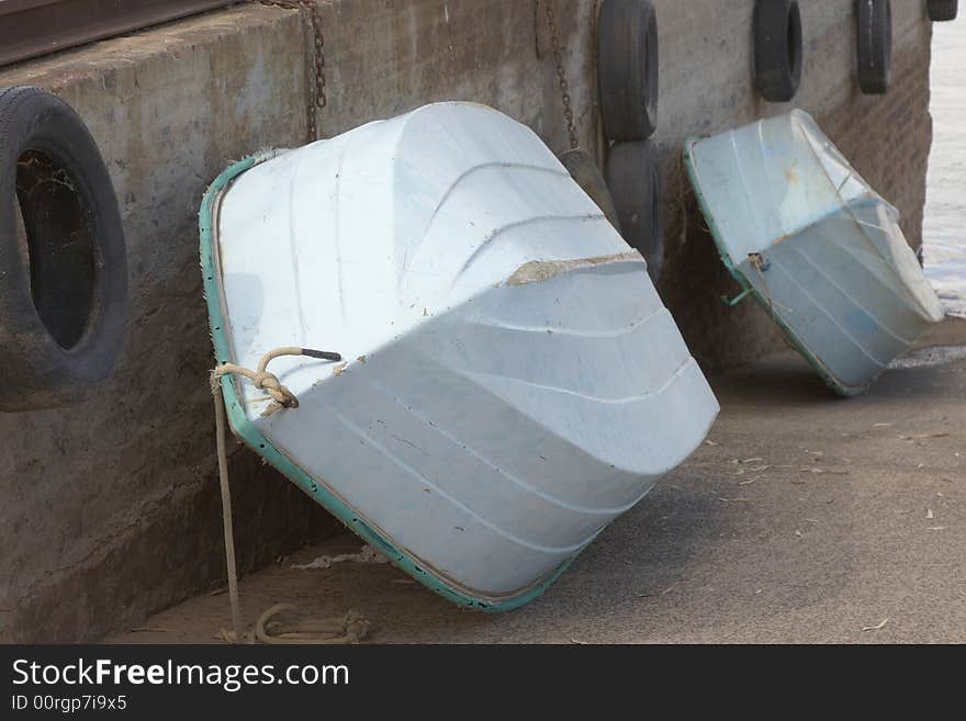 Small white and Jade Fishingboats with rope  in a row against sement wall with tyres and chains. Small white and Jade Fishingboats with rope  in a row against sement wall with tyres and chains