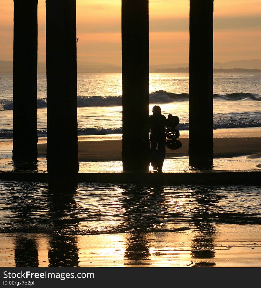 Lone figure standing on beach under pier as sun sets. Lone figure standing on beach under pier as sun sets