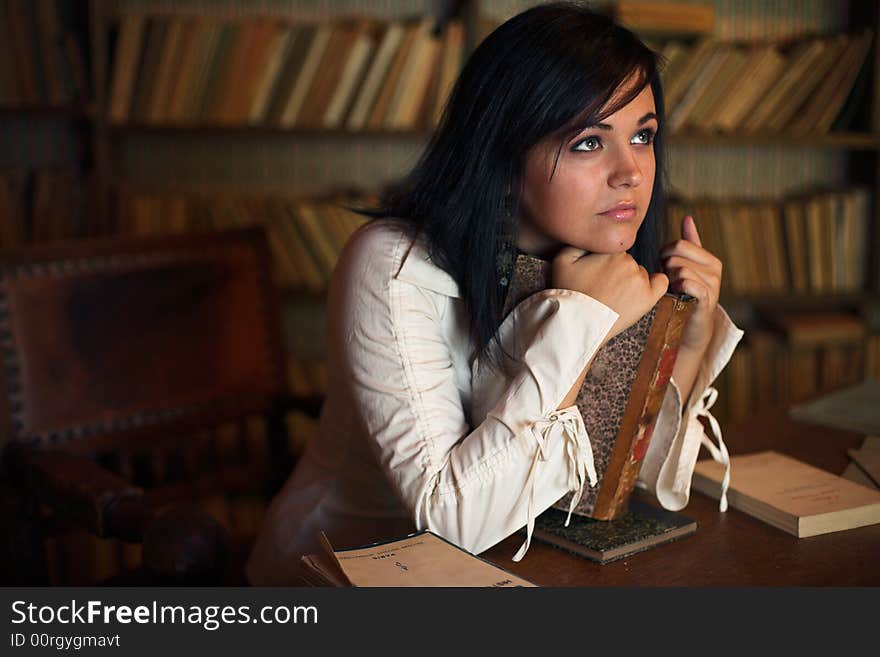 Woman thinking in library with an old book. Woman thinking in library with an old book