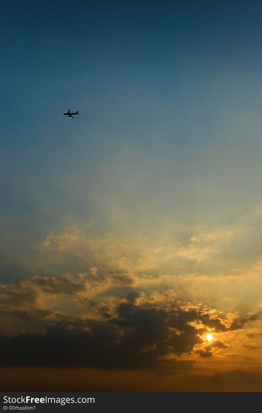 An aeroplane silhouetted in the sky as the sun rises over the horizon, partly obscured by low altitude clouds. An aeroplane silhouetted in the sky as the sun rises over the horizon, partly obscured by low altitude clouds