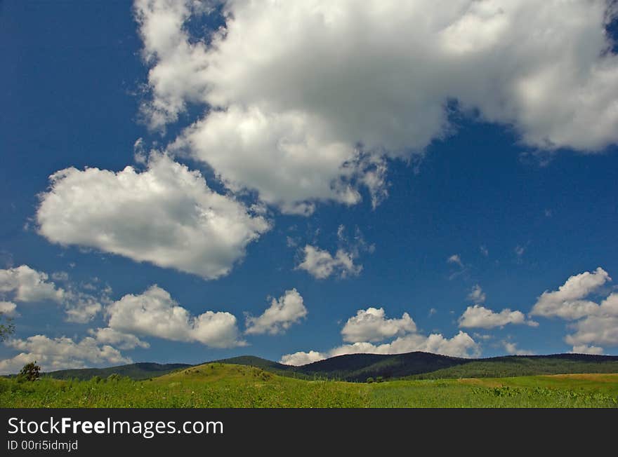 Big clouds on blue sky over green hill