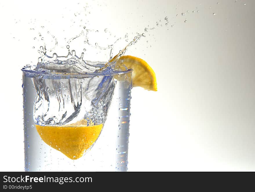 A lemon half splashing into a glass of water. A lemon half splashing into a glass of water.