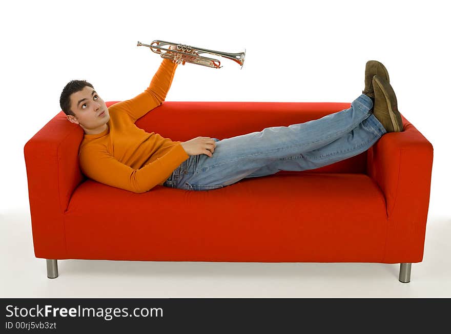 Thoughtful trumpeter lying on red couch and holding trumpet in hand. He's looking at something up. White background.