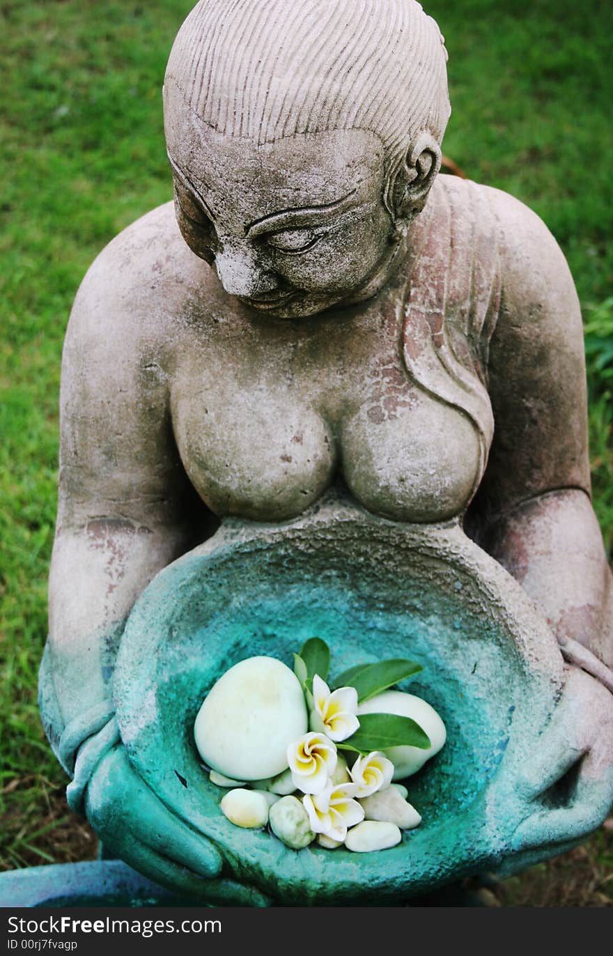 Asian statue holding a bowl of fragapani flowers - focus on the face.