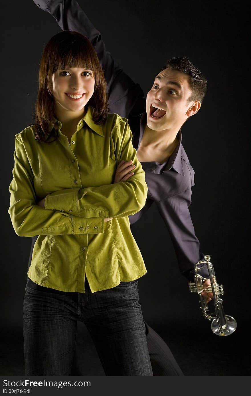 The man with trumpet wanted to surprise the woman. The man standing behind happy woman. She's looking at camera. Front view. The man with trumpet wanted to surprise the woman. The man standing behind happy woman. She's looking at camera. Front view.