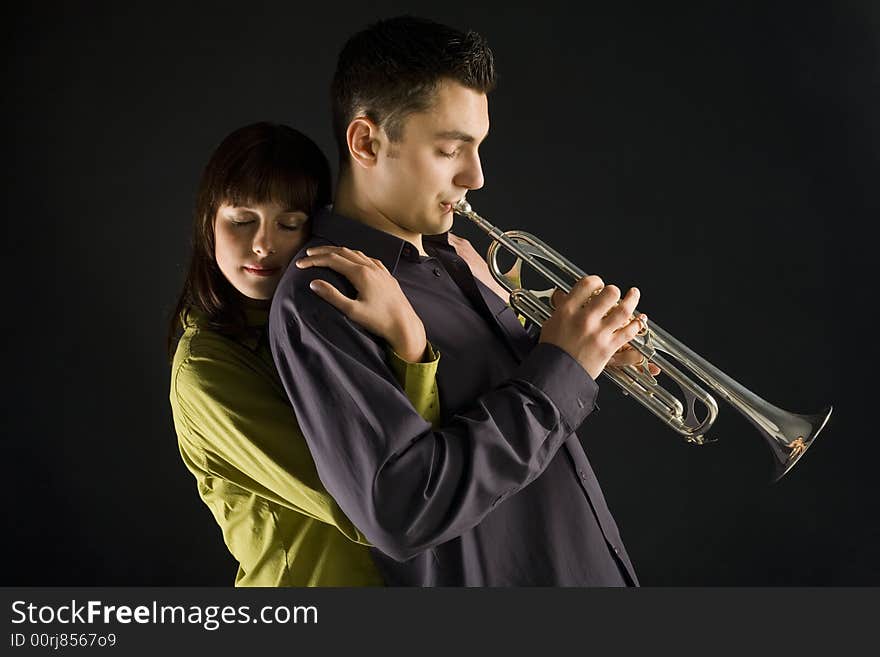 The woman huging the trumpet man. She standing behind the man. Side view. The woman huging the trumpet man. She standing behind the man. Side view.