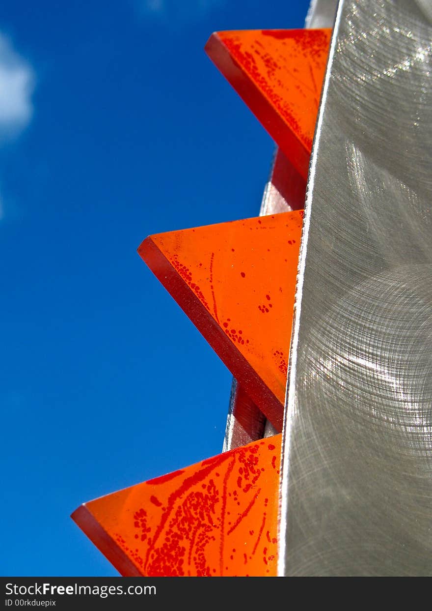 Abstract shot of orange and brushed aluminum set against a bright blue sky. Vertical format