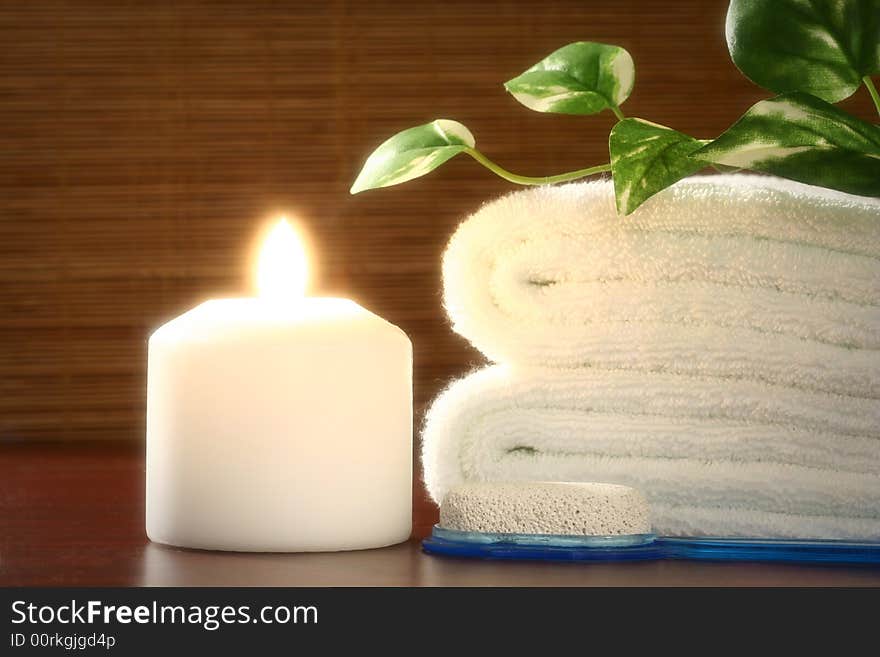 White candle and towel, green leaf and pumice in front of bamboo blind. White candle and towel, green leaf and pumice in front of bamboo blind