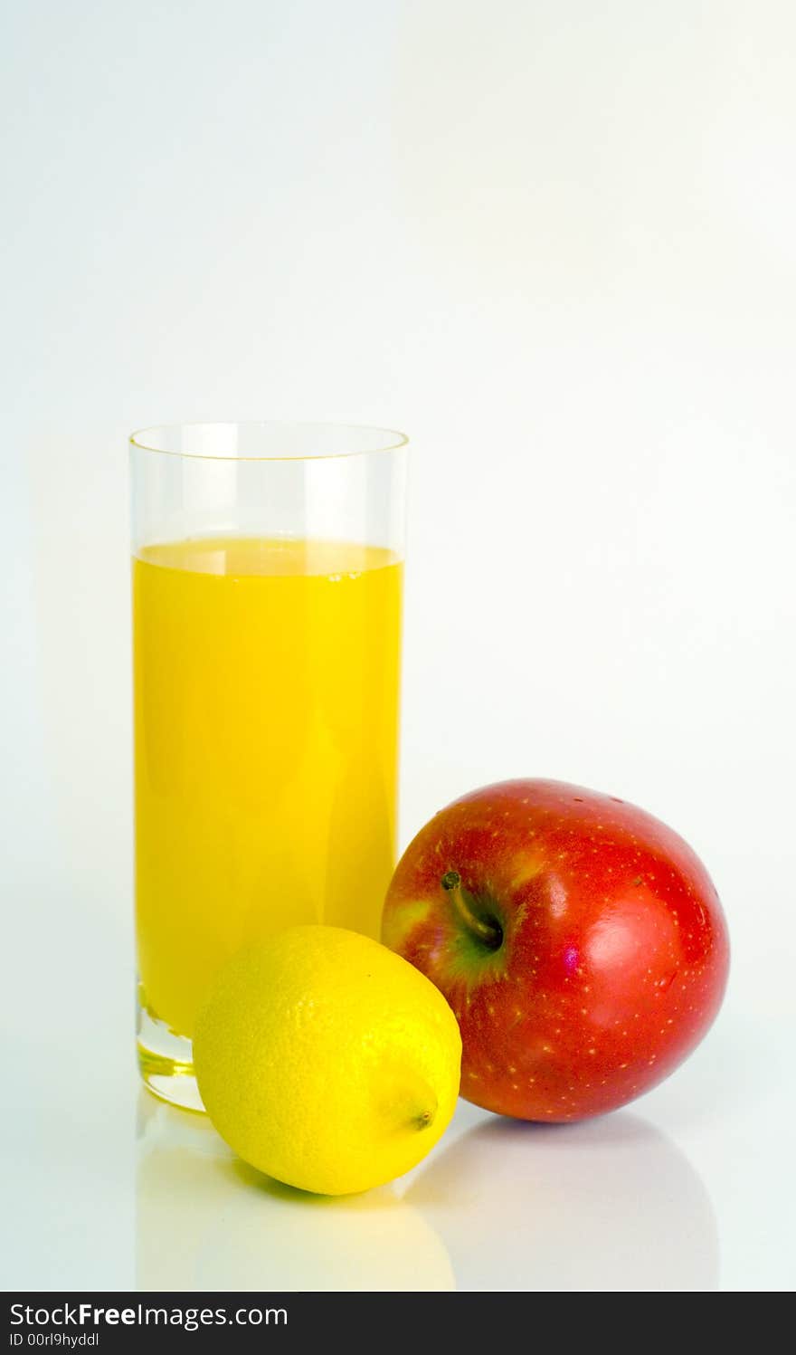 Big transparent glass of orange juice, yellow lemon, red apple on white background. Big transparent glass of orange juice, yellow lemon, red apple on white background