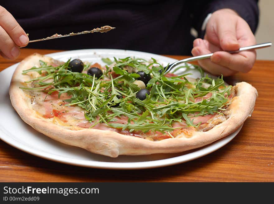 Vegetable pizza with ruccola and olives, mans hands holding  knife and fork, detail. Vegetable pizza with ruccola and olives, mans hands holding  knife and fork, detail.