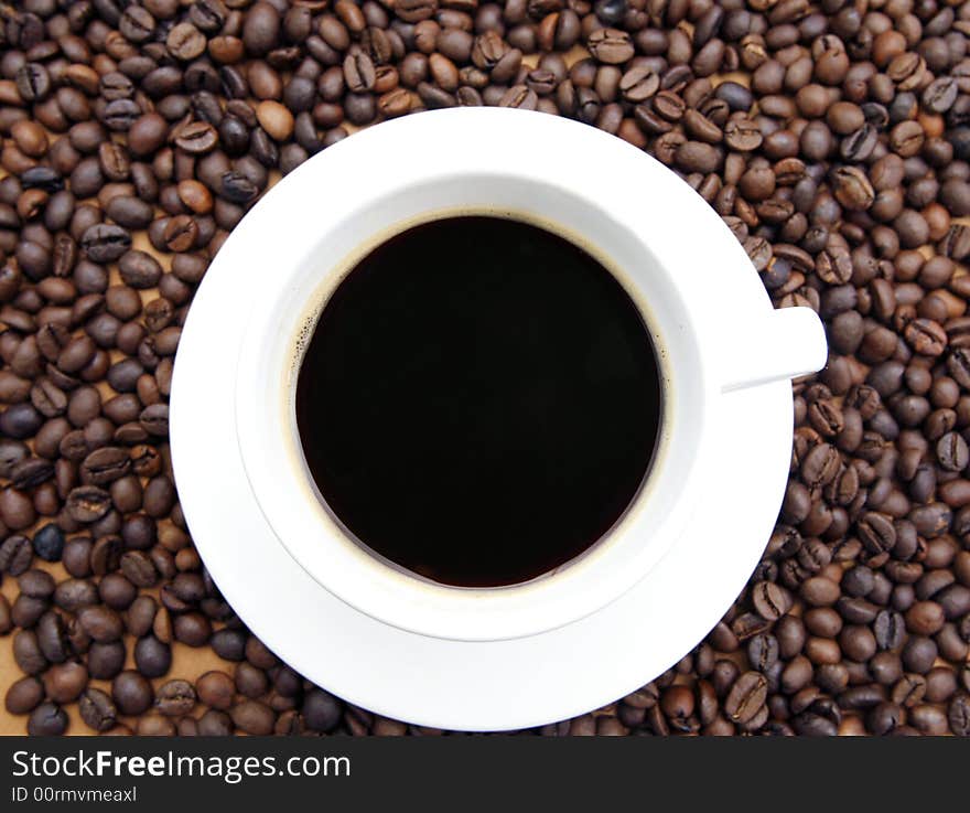 White coffee cup with black coffee and coffee beans on brown background