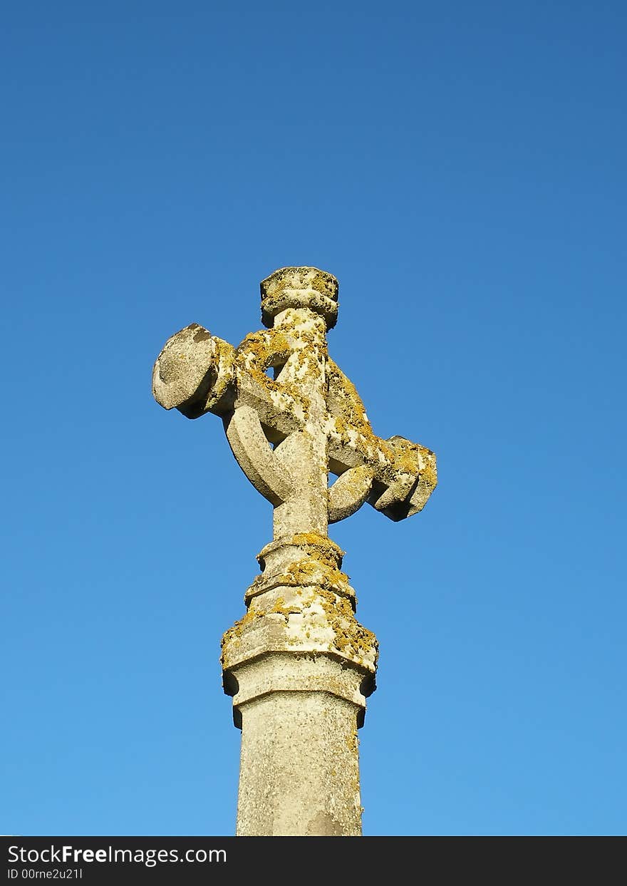 Lichen covered celtic cross set against blue sky