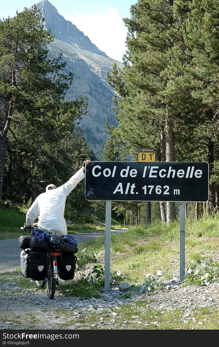 Exhausted fully loaded cyclist reaching a mountain pass in the Alps between France and Italy. Exhausted fully loaded cyclist reaching a mountain pass in the Alps between France and Italy.