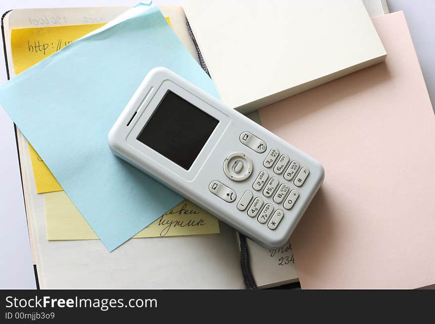 A white mobile phone placed against a notebook and colourful notes. A white mobile phone placed against a notebook and colourful notes