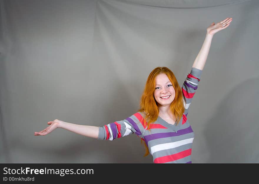 Portrait of young smiling woman with spreading hands on the gray background