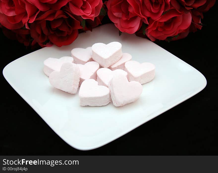 Plate of pink heart shaped marshmallows with roses on a black background. Plate of pink heart shaped marshmallows with roses on a black background.