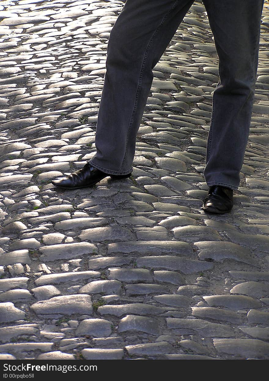 Jeans and black shoes on road from stones