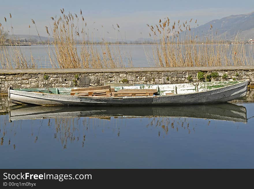 An old boat and its reflection on the water. grass, lake and the sky as background. An old boat and its reflection on the water. grass, lake and the sky as background