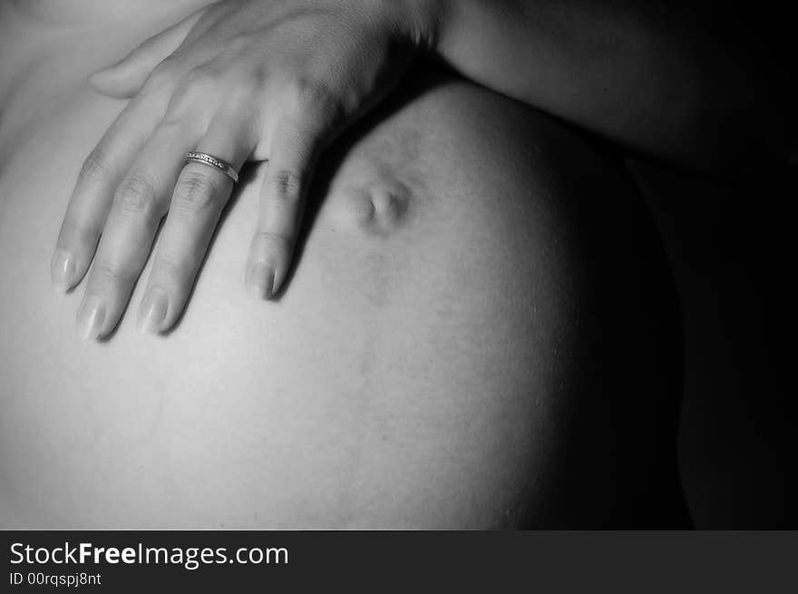 A pregnant woman wearing a wedding band places her hand over her belly. A pregnant woman wearing a wedding band places her hand over her belly.