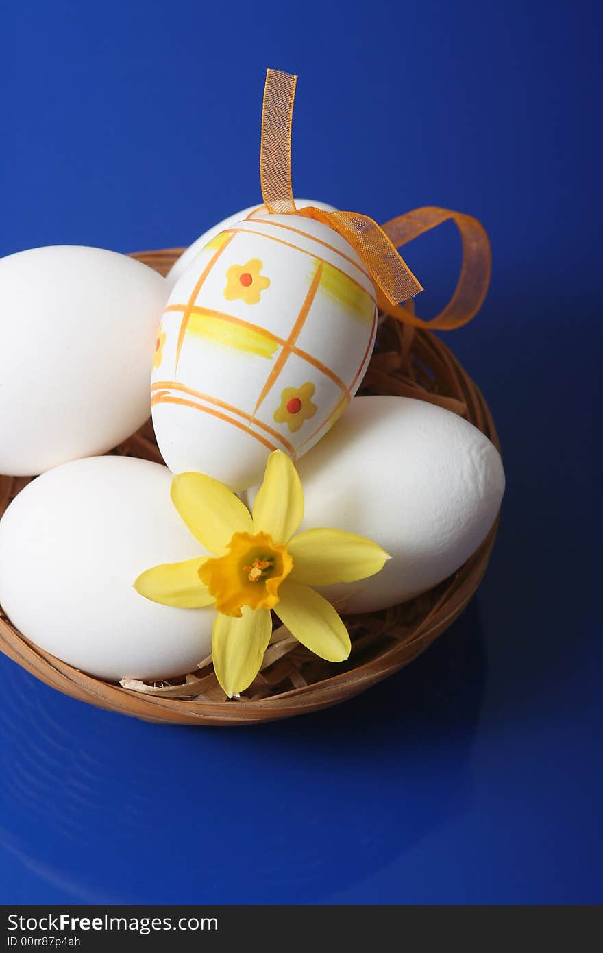 Easter eggs with yellow flower in basket on blue background.