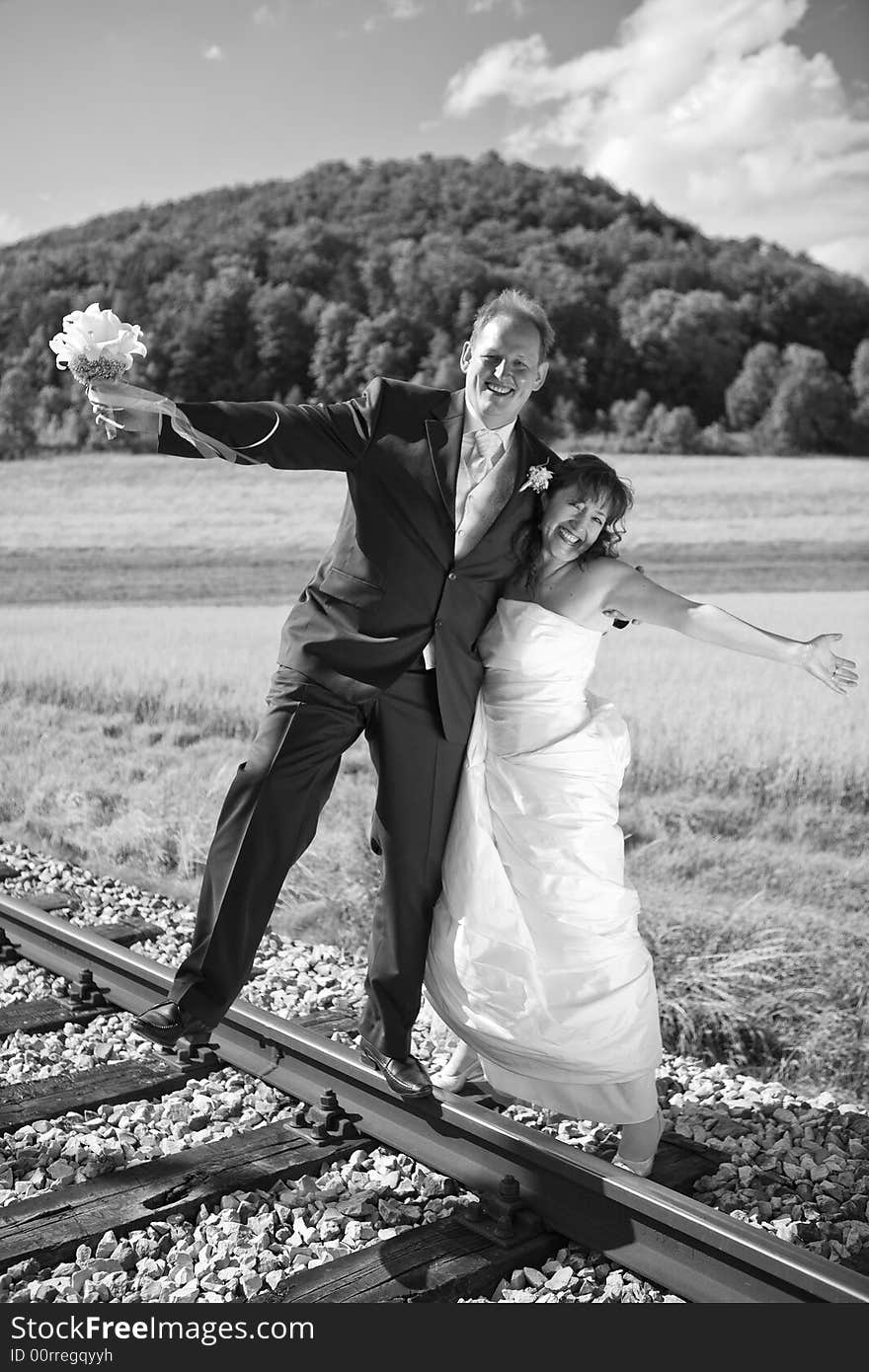 Bridal couple on rails, being in the nature. Great azure sky. Great summer! He balances with one foot on the rail. Black-white, monochrome. Bridal couple on rails, being in the nature. Great azure sky. Great summer! He balances with one foot on the rail. Black-white, monochrome.