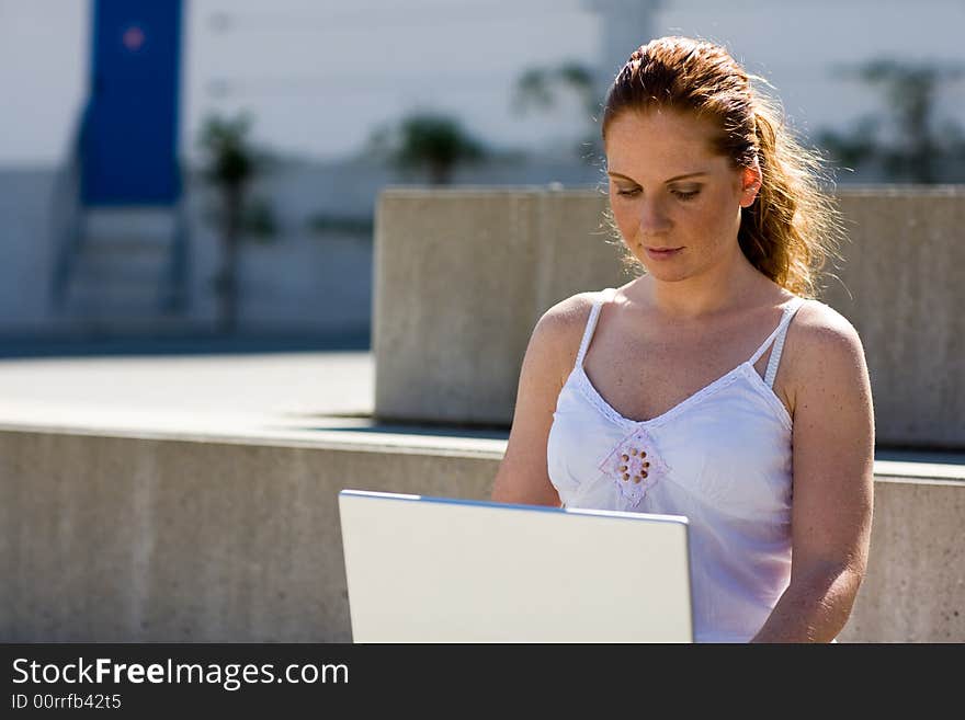 Woman (a scholar?) sitting alone on a stair, typing on the silver laptop. It's lightish and summery. Woman (a scholar?) sitting alone on a stair, typing on the silver laptop. It's lightish and summery.