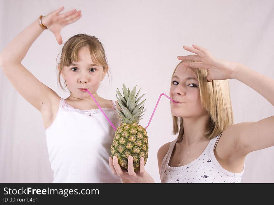 Two young girls with hands in the air   drinking from a pineapple. Two young girls with hands in the air   drinking from a pineapple