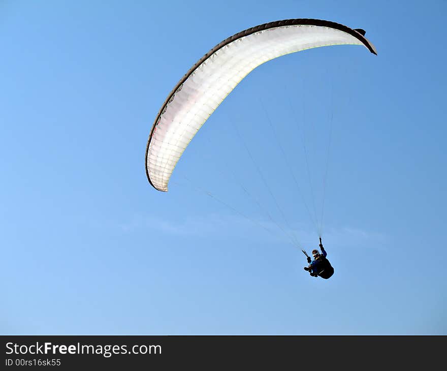 A paraglider is flying in the blue sky with his white paraglide. A paraglider is flying in the blue sky with his white paraglide