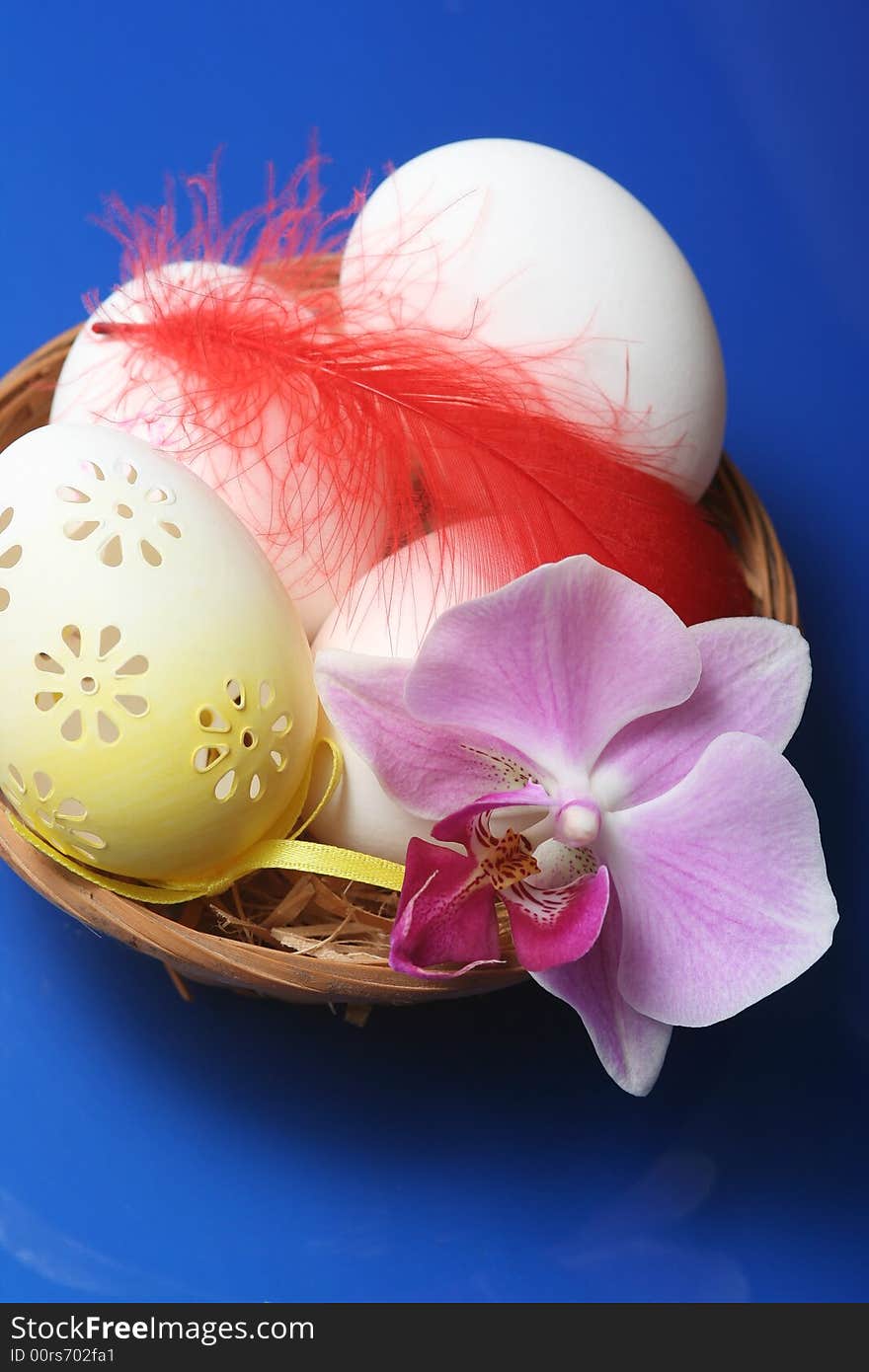 Easter eggs in basket with orchid on blue background.