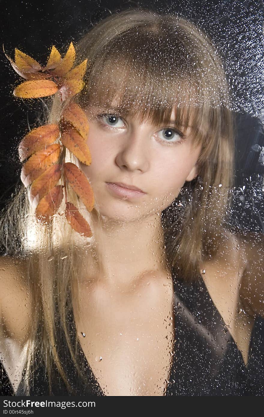 Beautiful young girl with leaves of a mountain ash behind glass