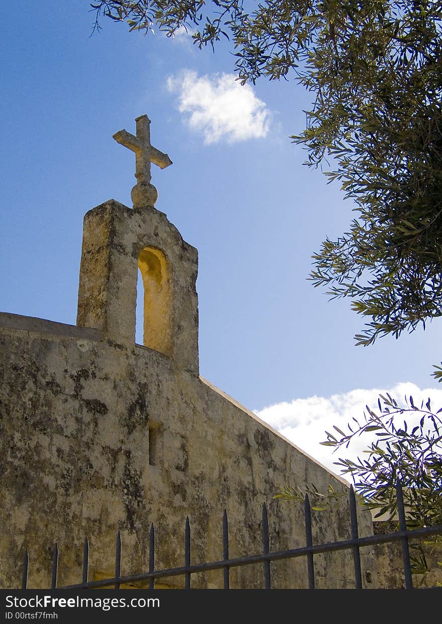 A limestone church against a blue sky framed by an olive tree. A limestone church against a blue sky framed by an olive tree