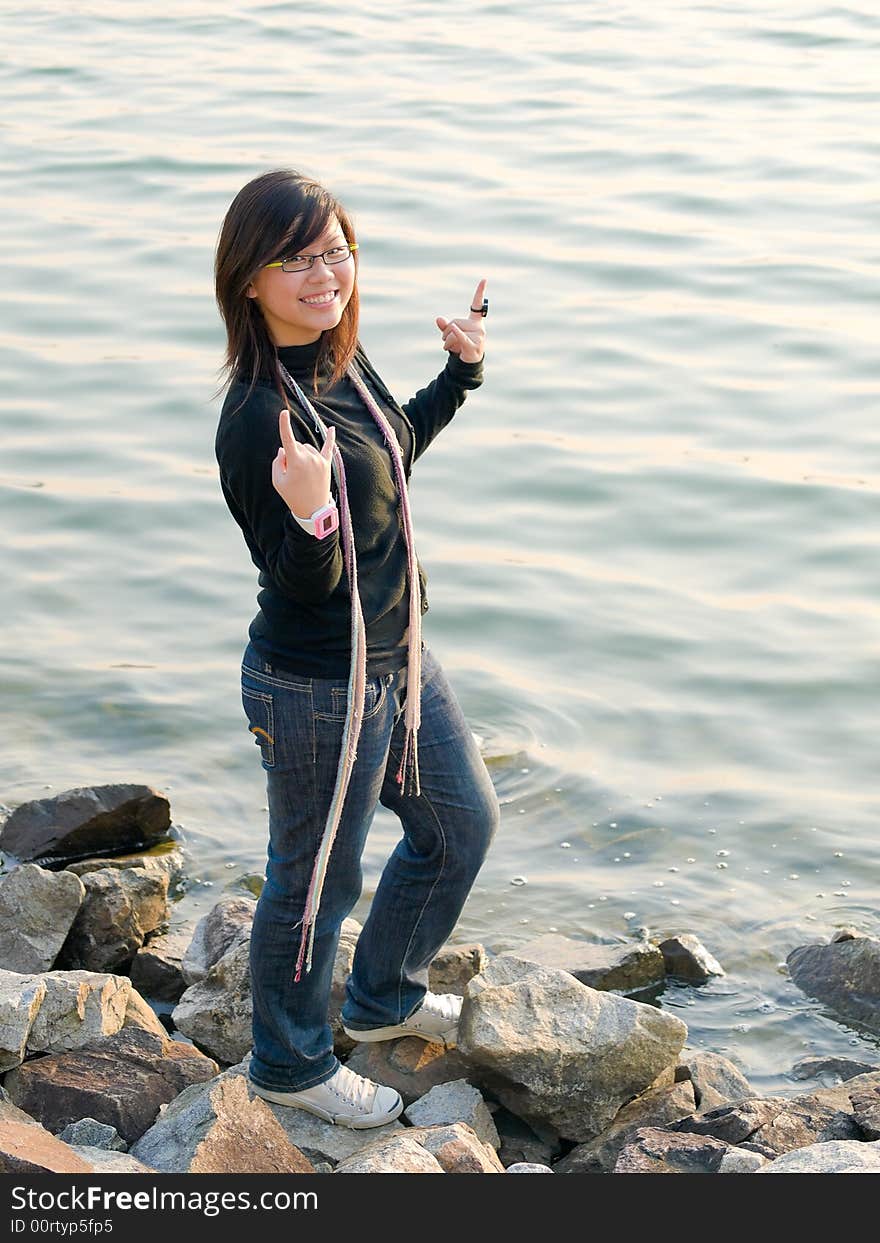 Teenager girl making hand signals with fingers at a rocky water's edge. Teenager girl making hand signals with fingers at a rocky water's edge