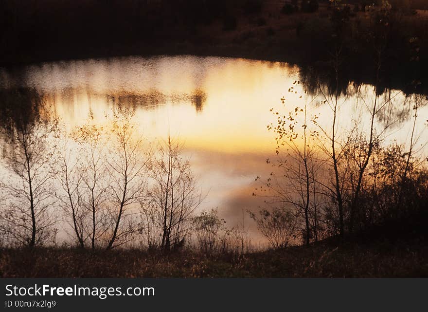 A calm pond with standing water sits idle in either dusk or dawn. A calm pond with standing water sits idle in either dusk or dawn